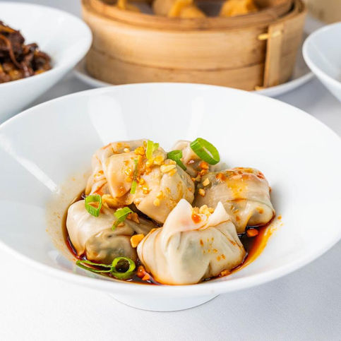 Delicious dumplings in a white bowl, fresh herbs, with other dishes.