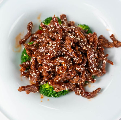 Beef strips with sesame seeds atop broccoli in a white bowl.