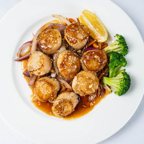 Seared scallops on a white plate with lemon, onions, and broccoli