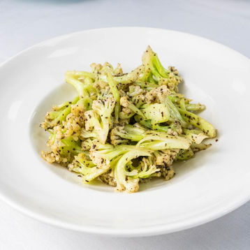 Overhead shot of a white plate with roasted cauliflower and seasoning