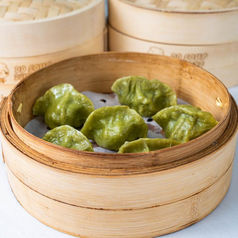Steaming bamboo basket of green dumplings, fresh and ready to eat.