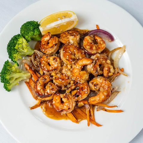 Grilled shrimp with vegetables and a lemon wedge on a white plate